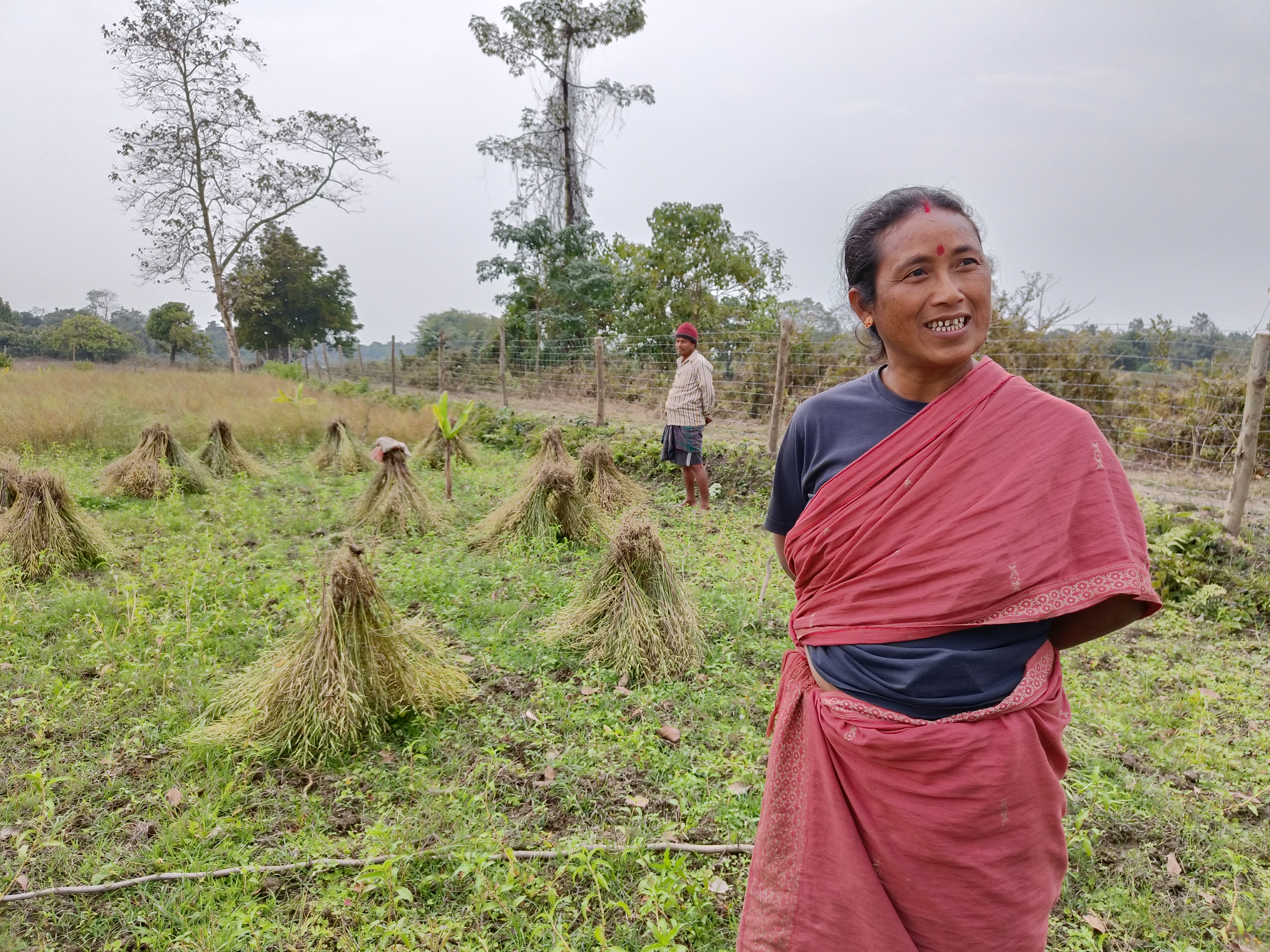 Kohinoor Gogoi stands in her mustard field, with her husband Uttam Gogoi in the background
